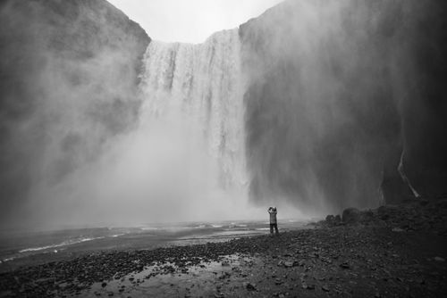 Iceland Travel Photography Tourist taking a photo in the spray at Skogafoss Waterfall Skogar South Region Sudurland Iceland