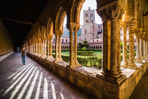 Italy Sicily Travel Photography Tourist at Monreale Cathedral Duomo di Monreale walking through columns in the courtyard gardens at sunset Monreale near Palermo Sicily Italy Europe