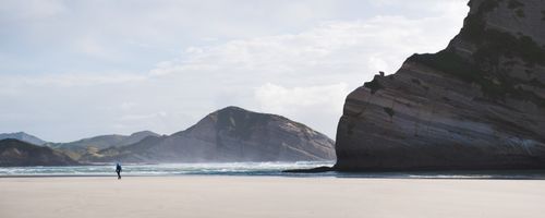 New Zealand Travel Photography Panoramic Photo of a Backpacker Walking Along Deserted Windy Wharariki Beach Golden Bay South Island New Zealand