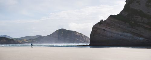 Landscape Photography by Professional Freelance UK Landscape Photographer Panoramic Photo of a Backpacker Walking Along Deserted Windy Wharariki Beach Golden Bay South Island New Zealand