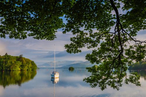 Landscape Photography by Professional Freelance UK Landscape Photographer Sailing boat floating on Lake Windermere at sunrise Lake District National Park Landscape Cumbria England UK Europe